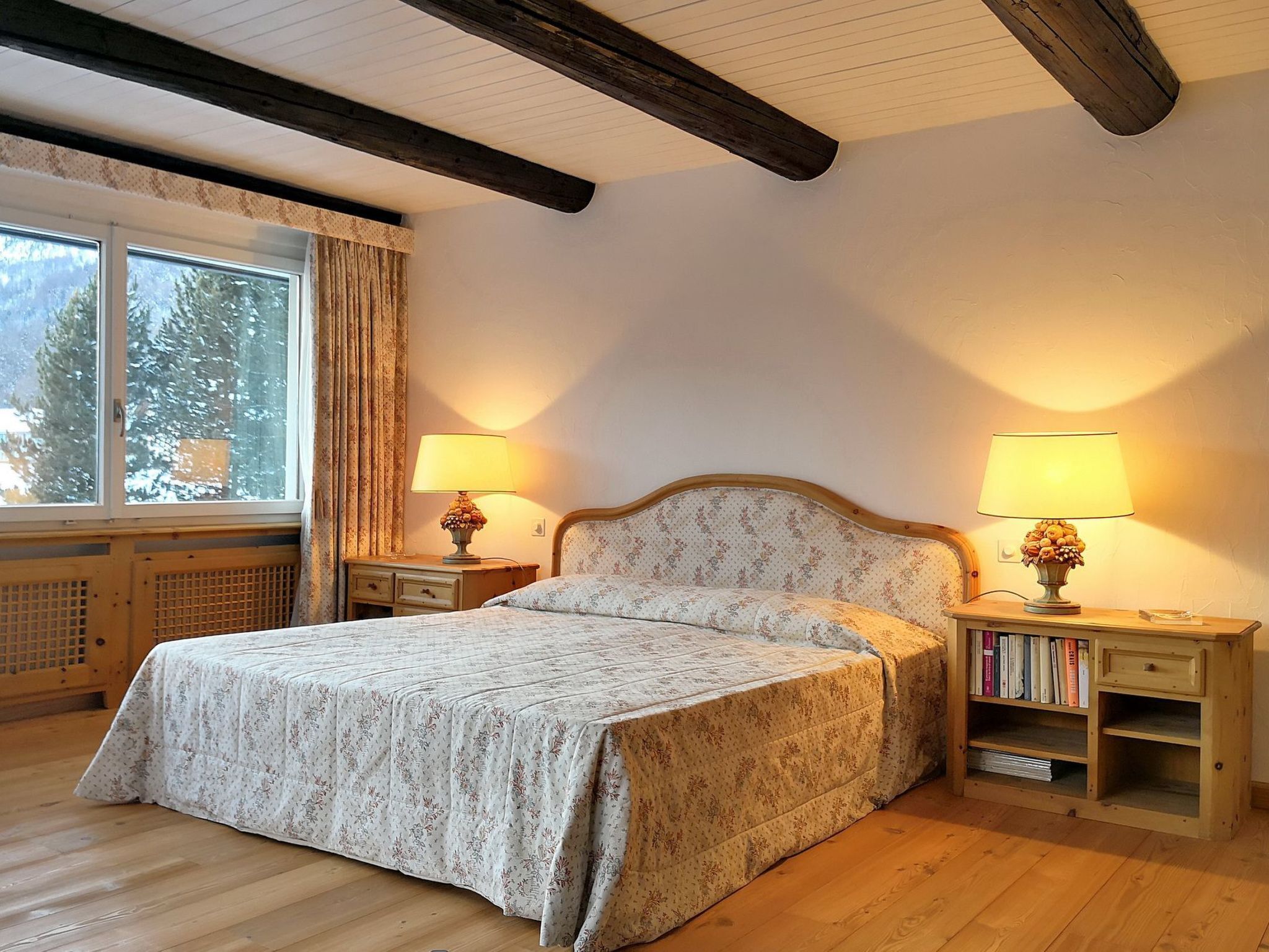 Een slaapkamer met een bed, twee nachtkastjes met lampen, een houten nachtkastje en een boekenplank.