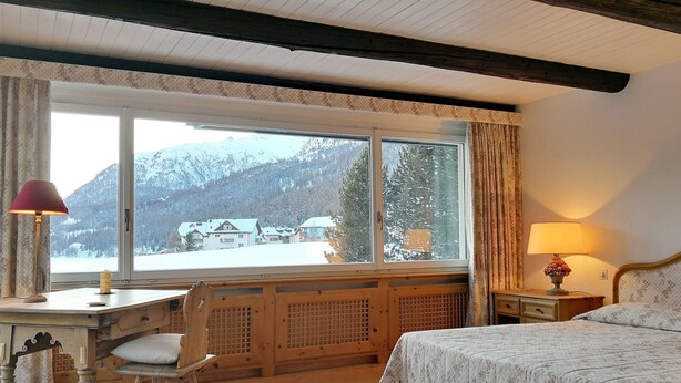 Een slaapkamer met een groot raam, een bed, een bureau en een stoel.