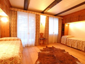 Ein Zimmer mit zwei Betten, Holzboden, Fellteppich und Vorhängen.