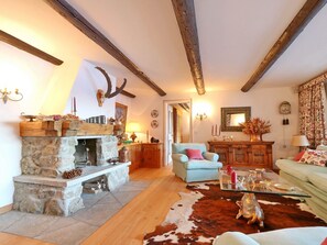 A rustic living room with exposed wooden beams, a stone fireplace, a cowhide rug, and a light blue sofa. - Apartment Muntagna Alva OG by Interhome (St. Moritz)