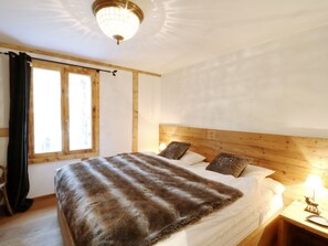 Ein Schlafzimmer mit Holz-Kopfteil, einem großen Bett mit Felldecke, zwei Kissen, einem Nachttisch mit Lampe und einem Fenster mit Vorhängen.