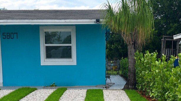 Uma casa com fachada azul, uma janela e entrada de cascalho com bordas de grama verde.