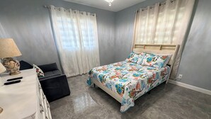 Quarto com cama, mesa de cabeceira, luminária, cômoda e janela com cortinas.