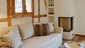 Una sala de estar acogedora con sofá, cojines, chimenea y una ventana con vigas de madera.