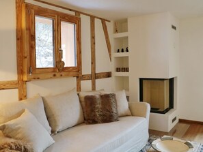 Ein gemütliches Wohnzimmer mit einer Couch, Kissen, einem Kamin und einem Fenster mit Holzbalken.