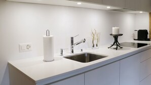 Una cocina moderna con encimera blanca, pileta de acero inoxidable y grifo negro.