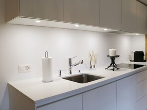 Eine moderne Küche mit weißer Arbeitsplatte, Spüle aus Edelstahl und einem schwarzen Wasserhahn.