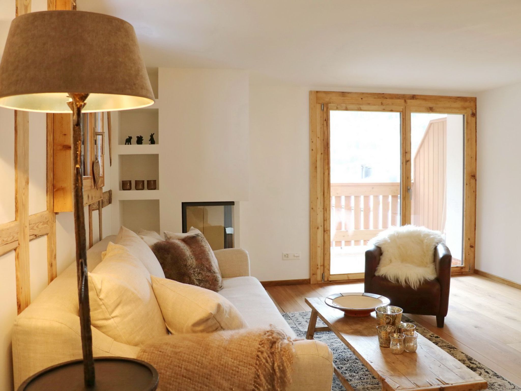 Una sala de estar acogedora con un sofá, una mesa de centro, una lámpara y vistas a una terraza de madera a través de una puerta de cristal.