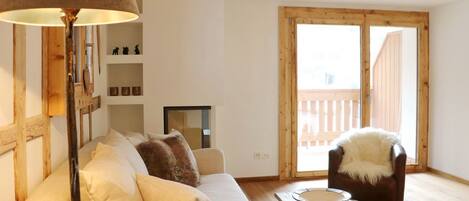 Una sala de estar acogedora con un sofá, una mesa de centro, una lámpara y vistas a una terraza de madera a través de una puerta de cristal.