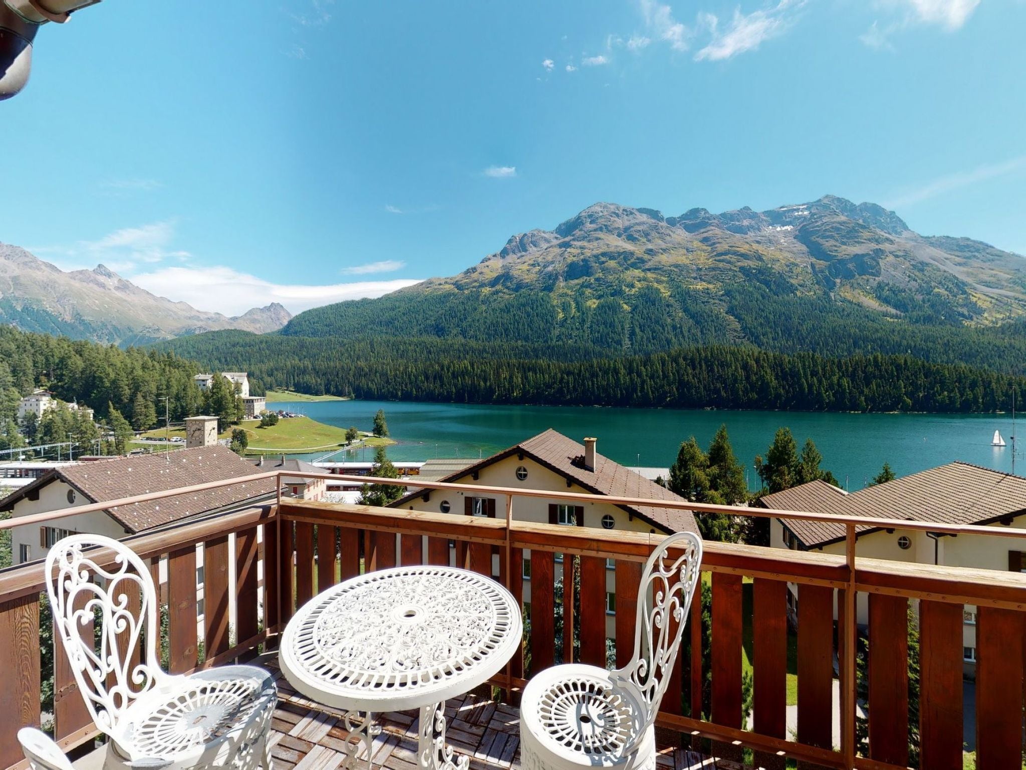 A balcony with a table and chairs overlooking a lake and mountains.