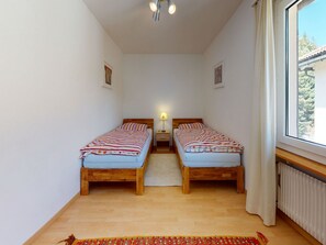 A room with two wooden beds, a small table, a lamp, and a window with curtains. - Apartment Giand Alva by Interhome (St. Moritz)