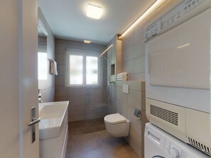 A modern bathroom with a bathtub, toilet, and stacked washer-dryer unit. - Apartment Giand Alva by Interhome (St. Moritz)