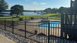 A swimming pool with a hot tub, surrounded by a fenced deck area with a view of a lake and distant buildings.