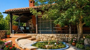 A patio with a stone pathway, a covered seating area, and a stone wall. - A house surrounded by forest. (Valtura)