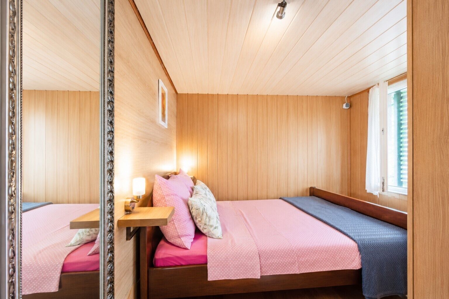 Una cabaña con dos camas de madera, una mesita de noche pequeña, un espejo y una ventana con cortinas.