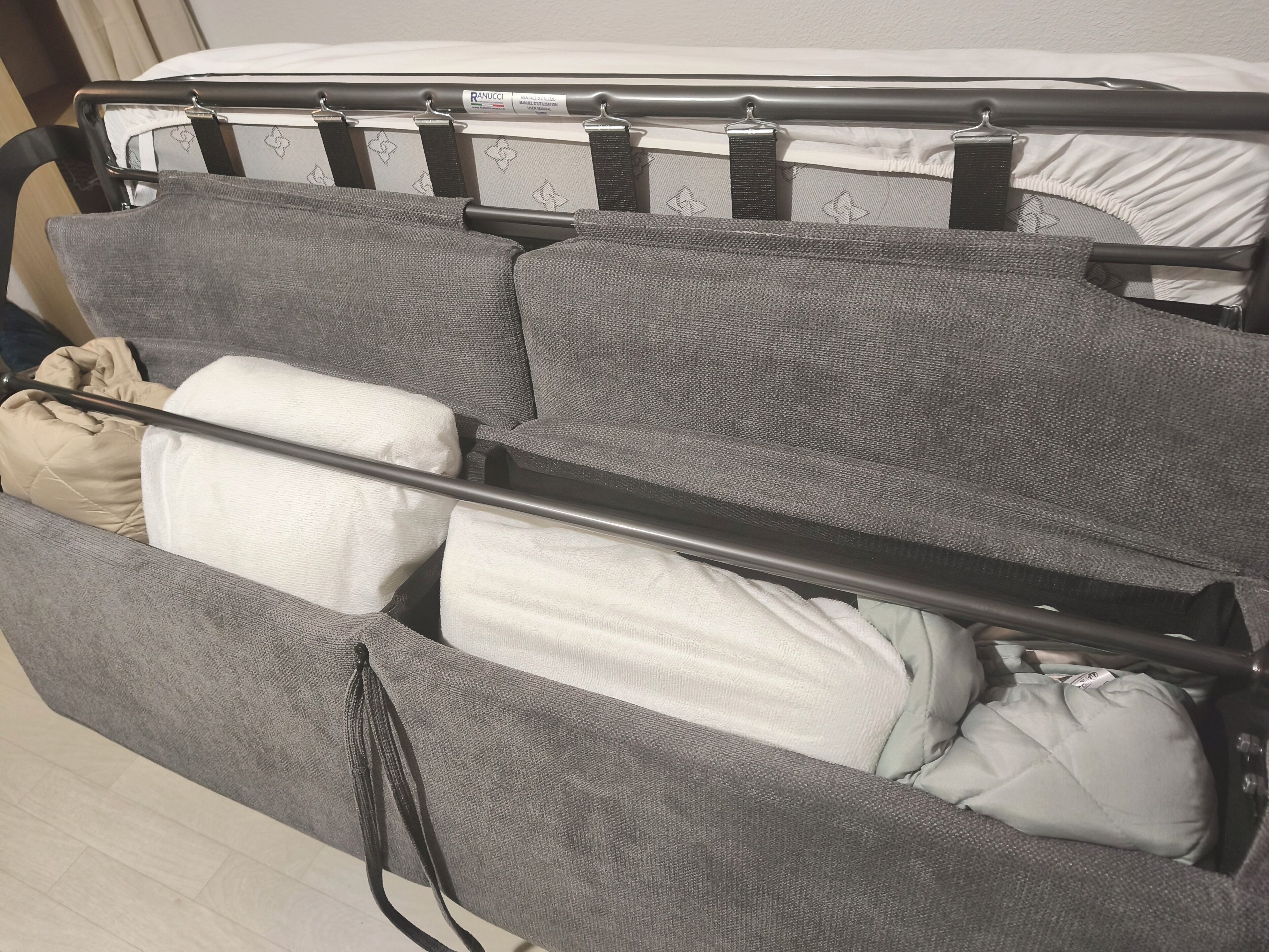 Un lit avec un cadre en métal, une tête de lit rembourrée de couleur grise et un oreiller blanc.