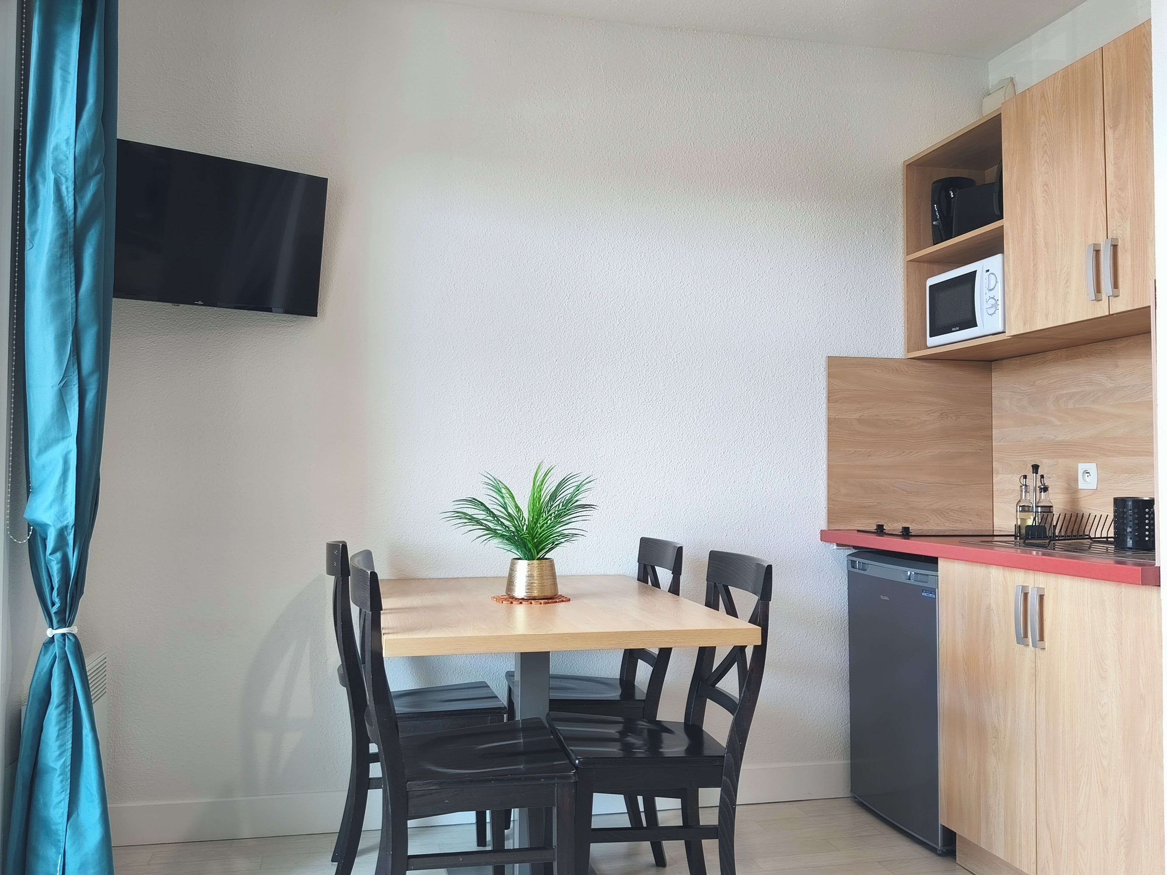 A compact kitchen with a dining table, chairs, a potted plant, a microwave, and a dishwasher.