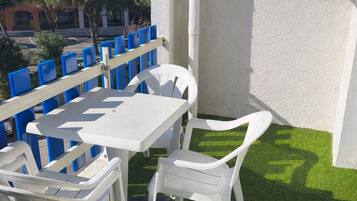 A balcony with a white table and chairs, artificial grass, and a view of buildings in the background.