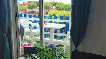 A room with a view of an outdoor area featuring a white table, a potted plant, and a blue curtain.