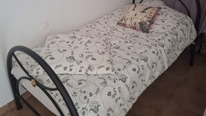 Ein kleines Einzelzimmer mit einem Bettgestell aus Metall, einer zudeckenden Bettdecke mit Blumenmuster, einem Kopfkissen, einem Wandbild und einem dekorativen Wandelement.