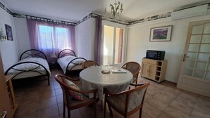 Ein kleiner, gut beleuchteter Raum mit zwei Betten, einem Esstisch mit Stühlen, einem Fernseher und einem Schrank.