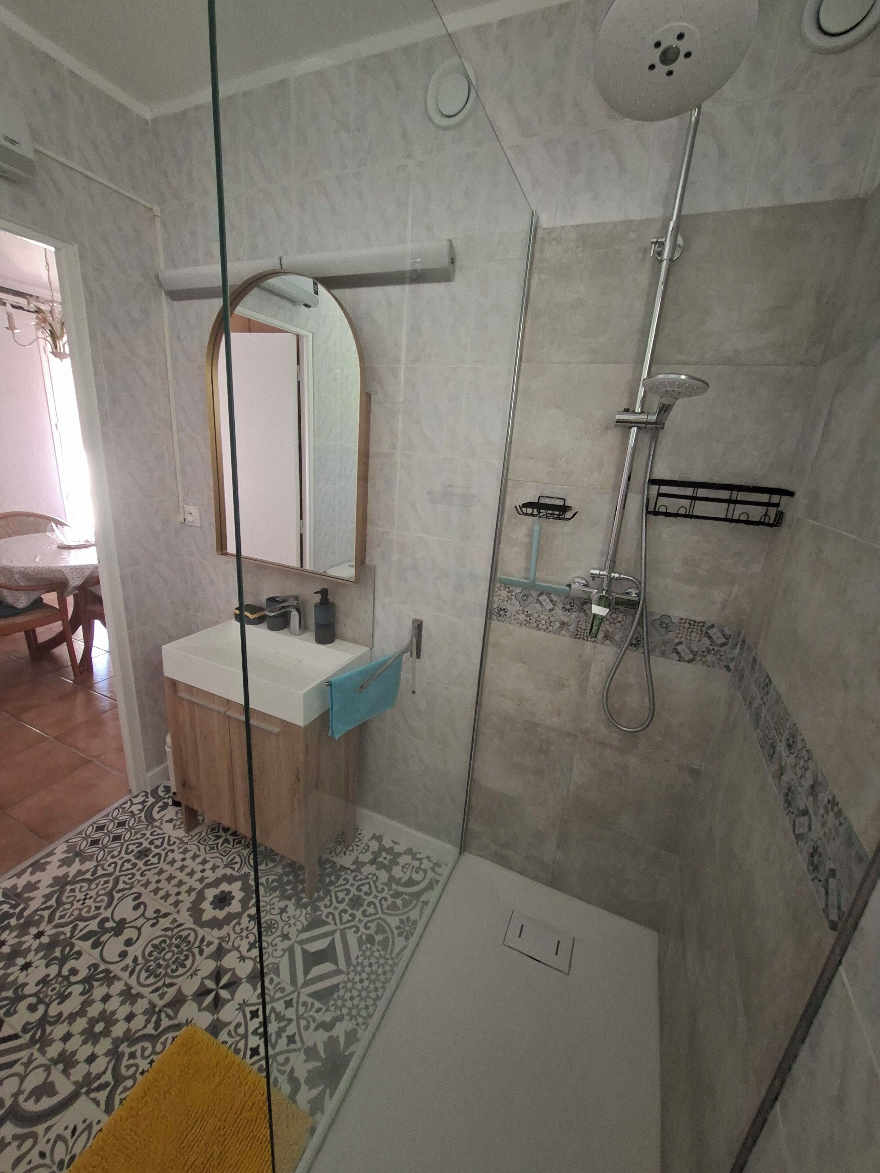 Un baño moderno con cabina de ducha de vidrio, un lavamanos blanco y un espejo encima.