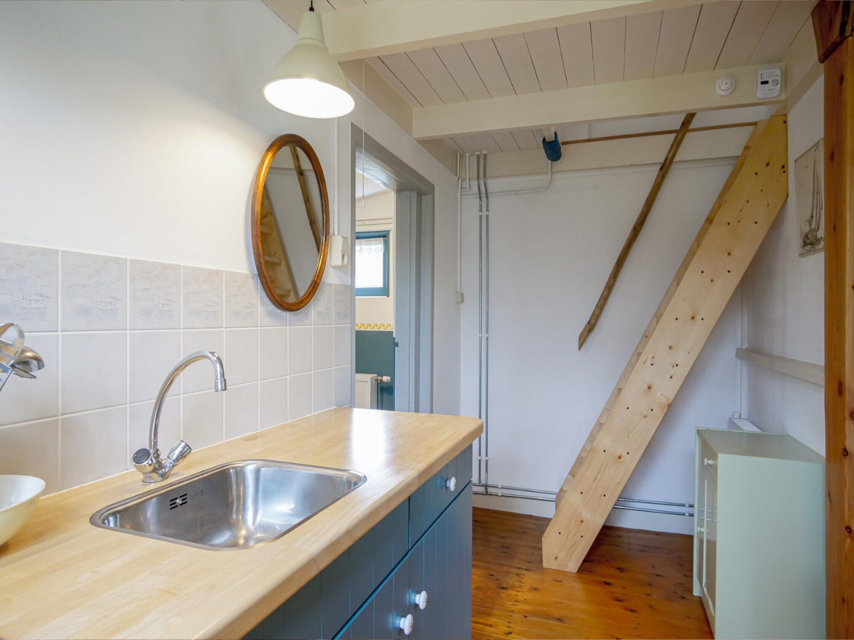 A kitchen with a double sink, wooden cabinets, a mirror, and a wooden staircase.