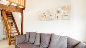 Ein Wohnzimmer mit einer Holztreppe, einem grauen Sofa und einem floralen Gemälde an der Wand.