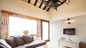 Ein modernes Wohnzimmer mit einer Couch, einem Couchtisch, einem Fernseher und einer dekorativen Deckenleuchte.
