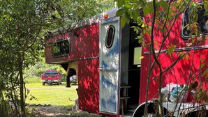 A gravel path leading to a red and blue camper with a truck parked in the background.