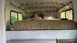 A bed with a patterned cover, two pillows, and a blanket in a room with windows and string lights.