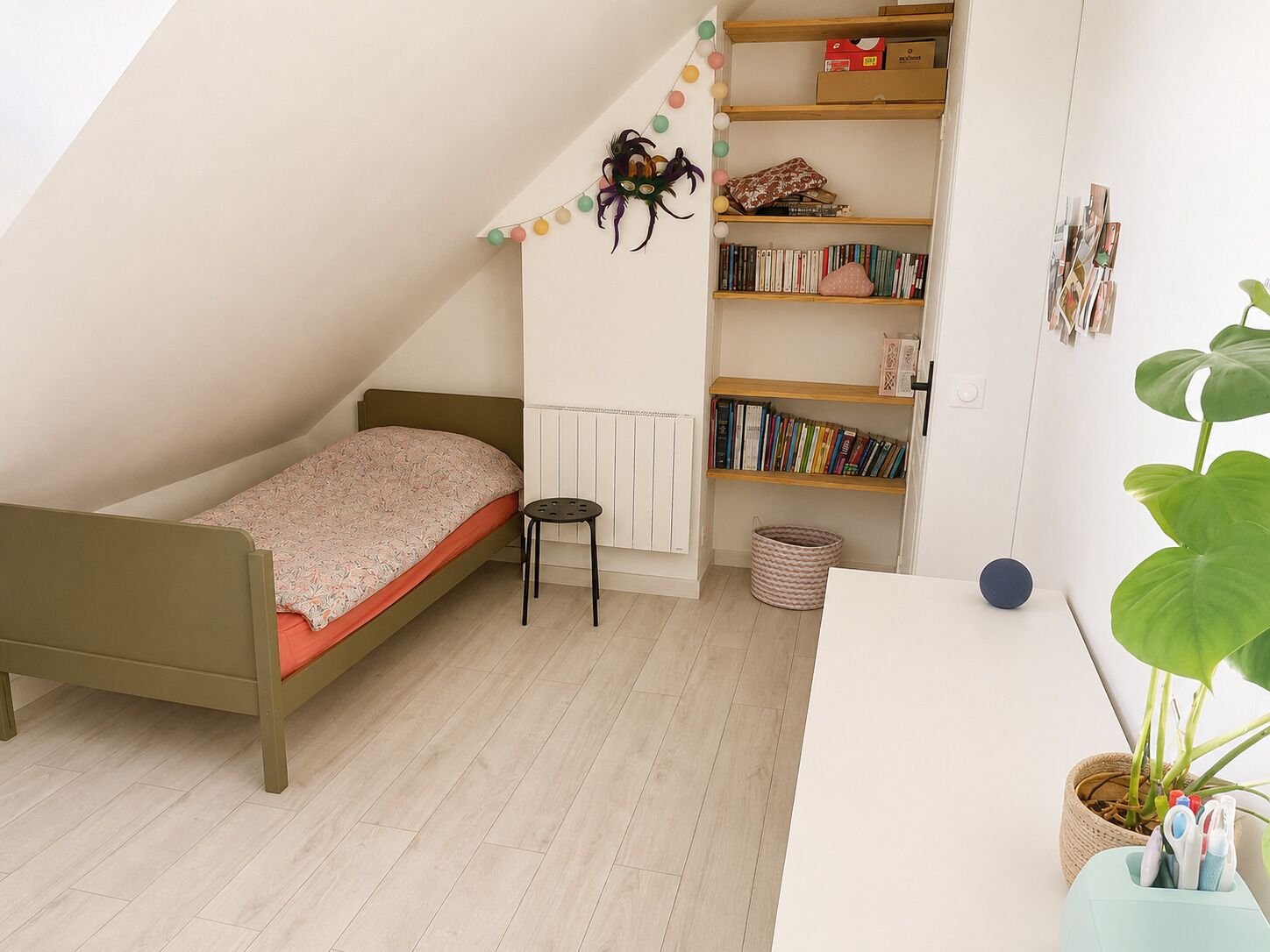 Une chambre à coucher avec un lit, une petite table, une bibliothèque, un radiateur et une plante en pot.