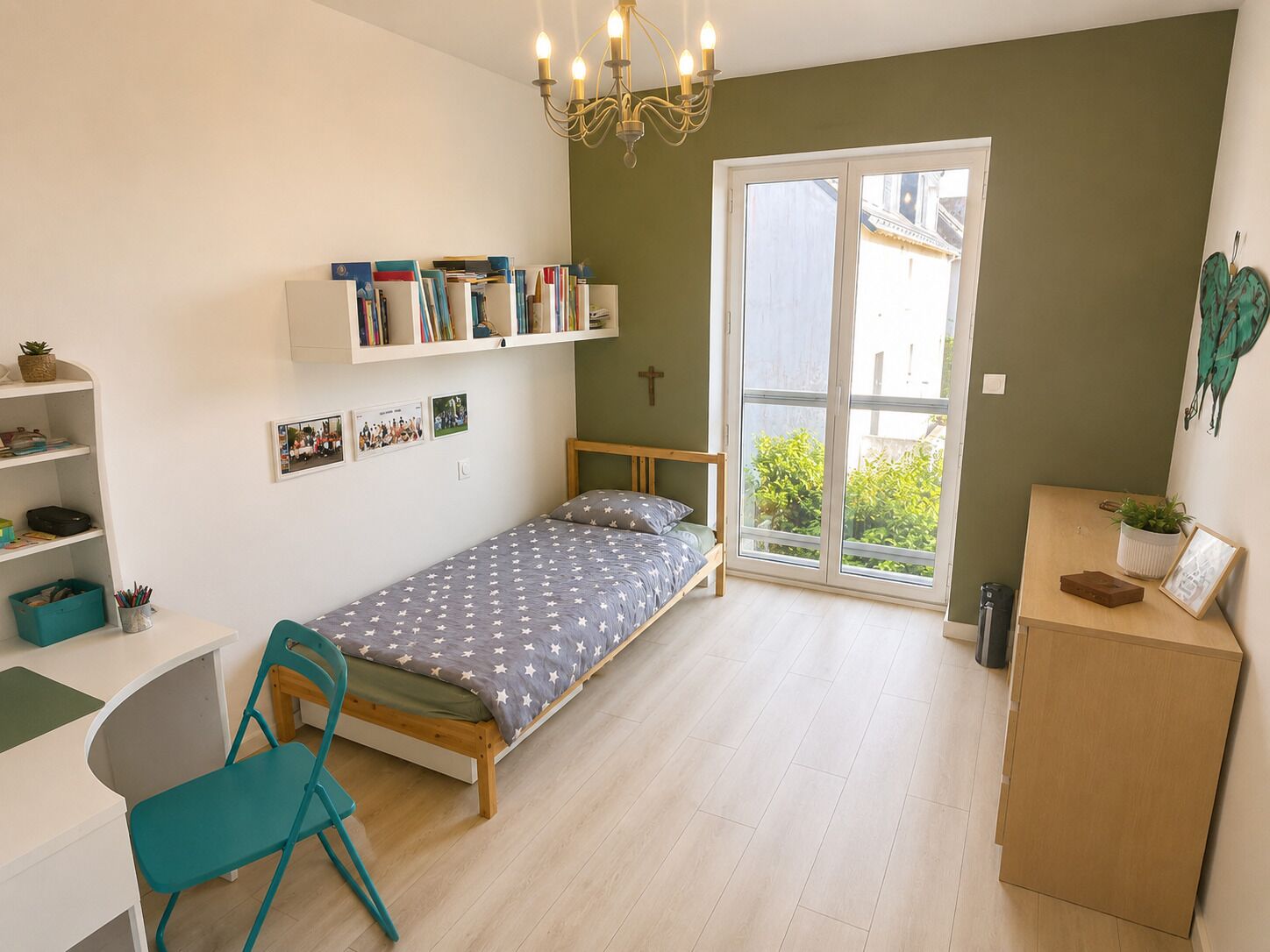 Quarto pequeno e bem iluminado com uma cama, escrivaninha, cadeira, estante e porta de vidro corria para área externa.