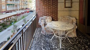 En balkon med et marmorbord og stole, en murstensvæg samt udsigt til en gade med udendørs siddepladser.