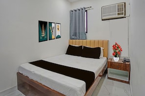 A bedroom with a bed, a nightstand, a wall-mounted air conditioner, and artwork on the wall. - Premium Hotel G.N Palace (Kolkata)