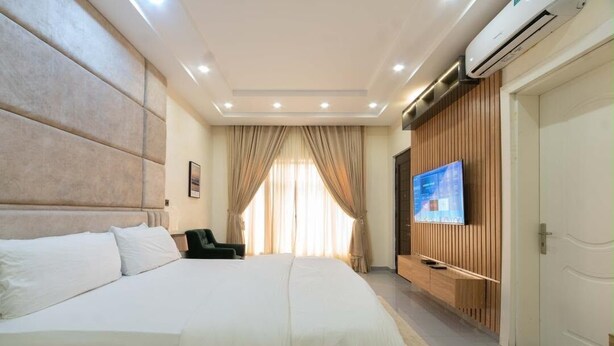 A hotel room with a large bed, a TV mounted on the wall, and a wooden panel wall. - Beautiful Waterfront 4-bedroom Terrace Duplex in vibrant Lekki (Lekki)