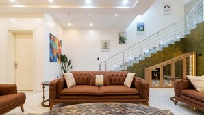 A modern living room with a brown sofa, a glass coffee table, and a staircase leading to an upper level. - Beautiful Waterfront 4-bedroom Terrace Duplex in vibrant Lekki (Lekki)