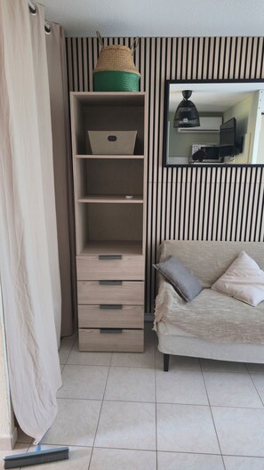 A room with a sofa, a wall-mounted TV, a shelf with storage boxes, a woven basket, and a broom on the floor. - Bormes-les-Mimosas—Quiet 4-bedroom home with AC, Wi-Fi, parking, and a basement, near the heart of La Favière (Bormes-les-Mimosas)
