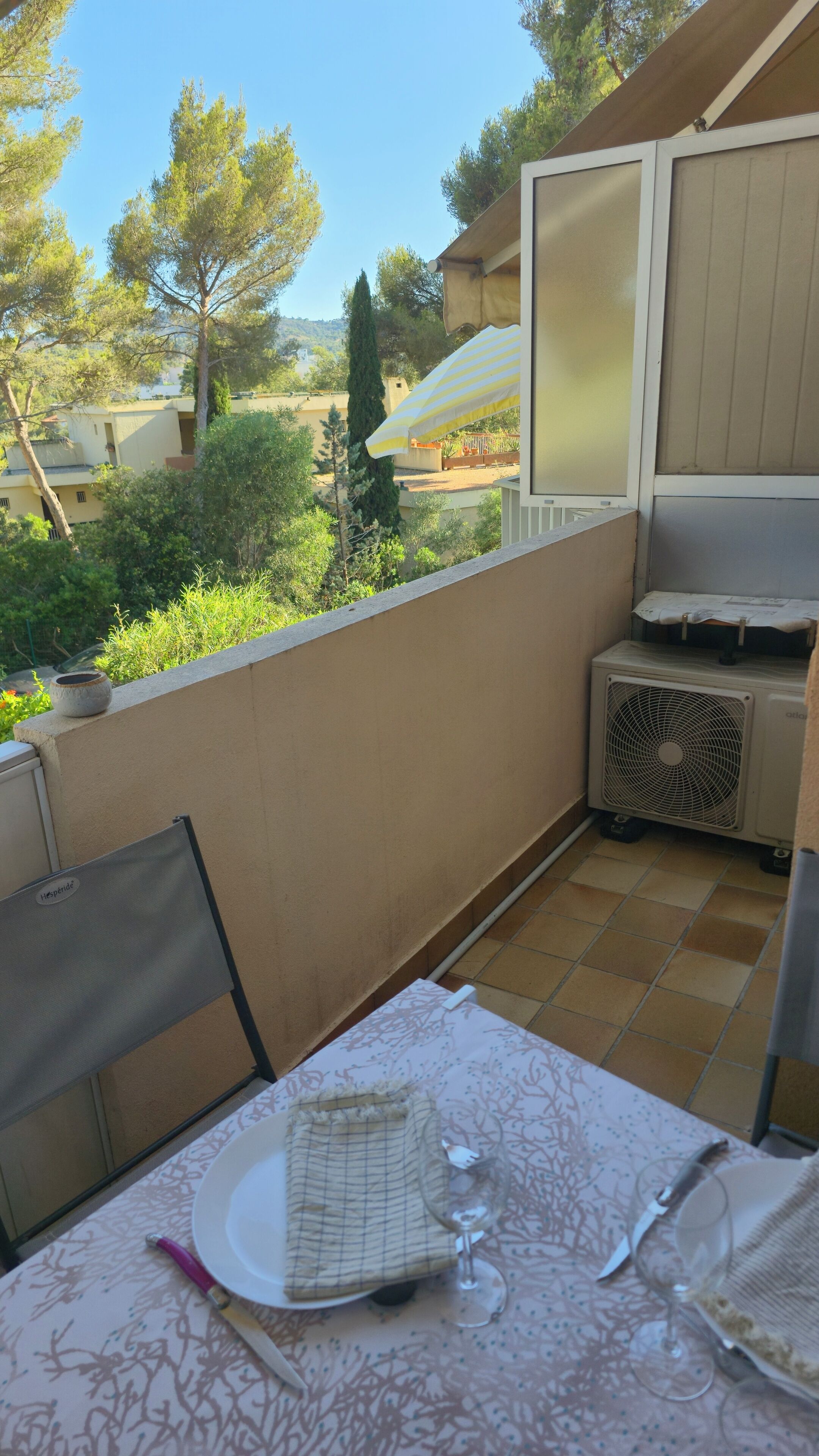 Un balcón con mesa lista para comer, un ventilador y vistas del entorno.