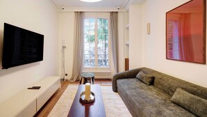 A living room with a flat-screen TV, a sofa, a coffee table, a window with curtains, and a radiator. - Cozy Appartement a/c 1br/2p- Montmartre (Paris)