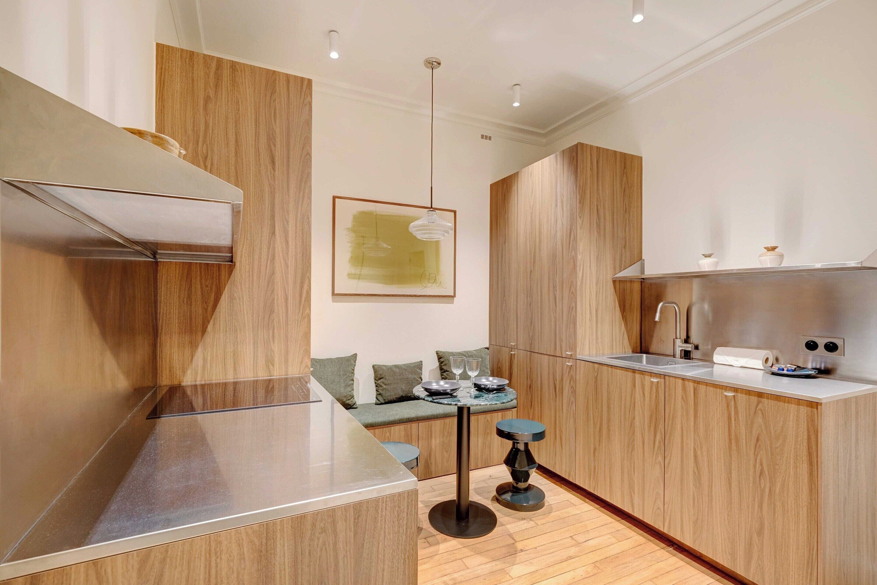 A modern kitchen with wooden cabinetry, a built-in stove, a dining area with a bench, and pendant lighting.