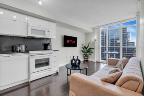 A modern kitchen with white appliances, a flat-screen TV, and a large window offering a city view.