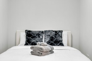 A neatly made bed with a folded towel stack and a black patterned pillow.