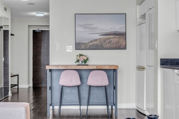 A modern kitchen with a wooden countertop, two pink bar stools, and a framed landscape picture on the wall.