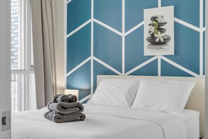 A neatly made bed with white linens, a stack of folded towels, and a wall with a geometric pattern. - The Perfect Downtown Stay Hotel|Steps to Jays, CN Tower & Waterfront W/Parking (Toronto)
