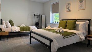 Une chambre avec deux lits, une fenêtre avec des plantes, un radiateur et des œuvres d’art accrochées au mur.