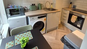 Une cuisine compacte équipée d’un lave-linge, d’un évier, d’un four à micro-ondes et d’un petit coin repas avec une table et des chaises.