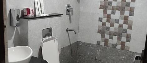 A bathroom with a toilet, a sink, a shelf with toiletries, and a shower area.