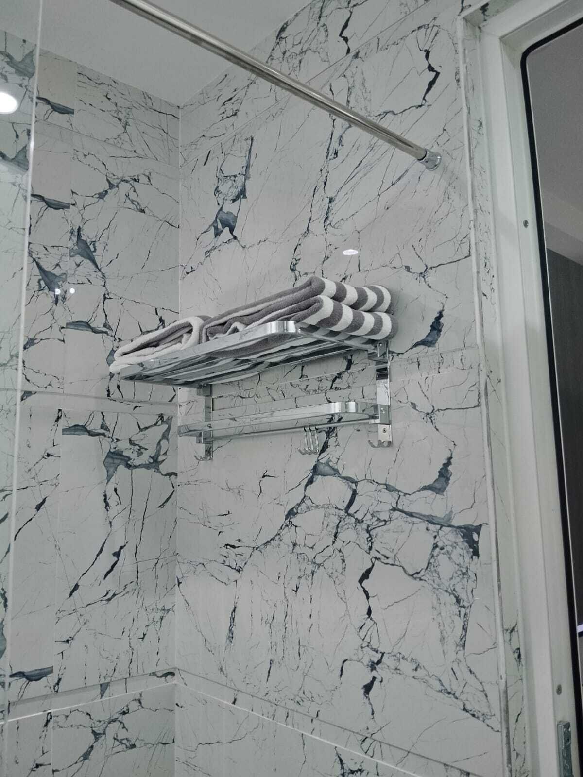 A bathroom with a marble wall, a towel rack, and a shower head.