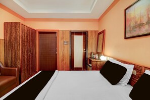 A hotel room with a bed, a desk with a lamp, a chair, and a wardrobe. - Classic Cherry City Cottage (Guwahati)